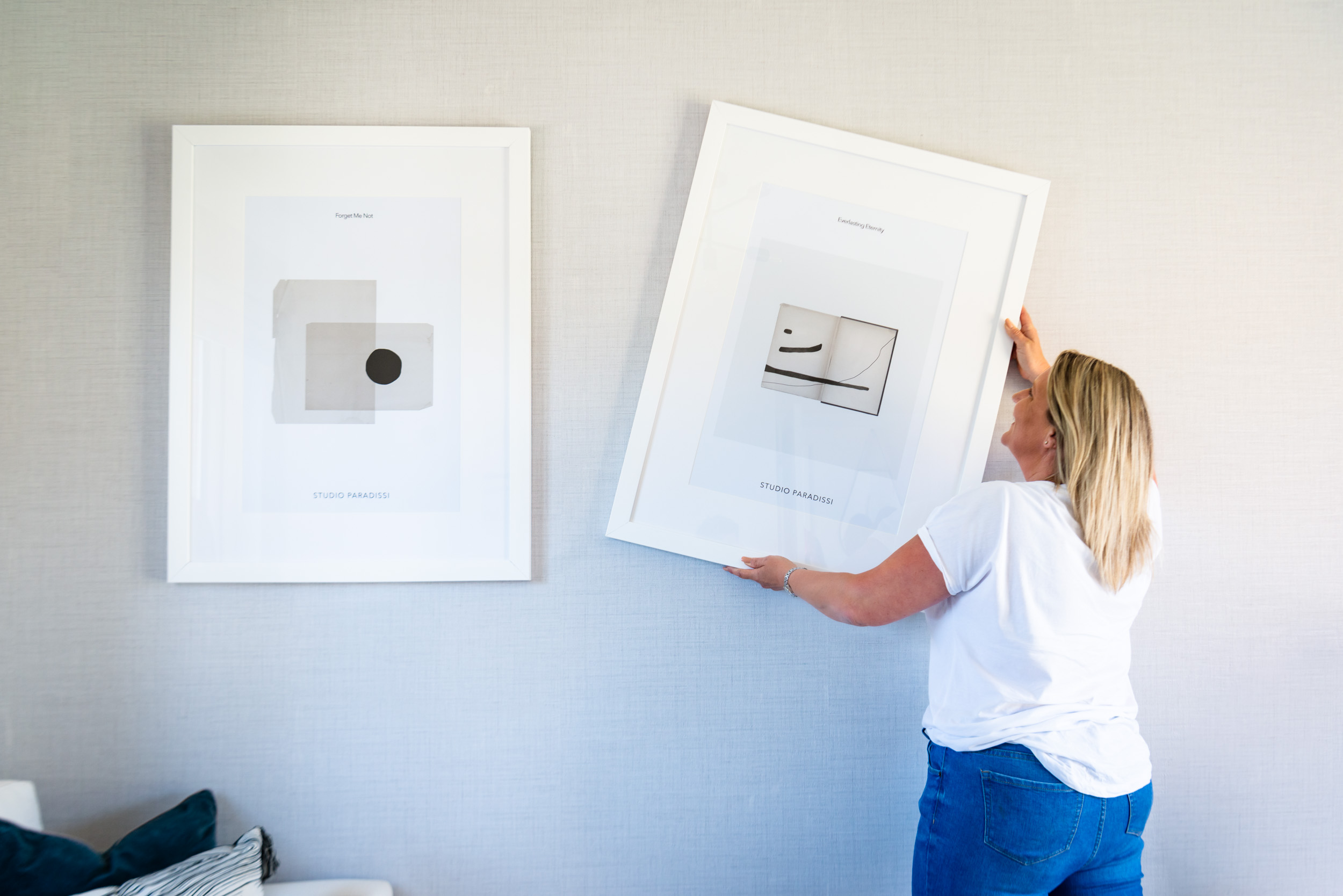 A lifestyle photo of a woman hanging a photo on the wall.